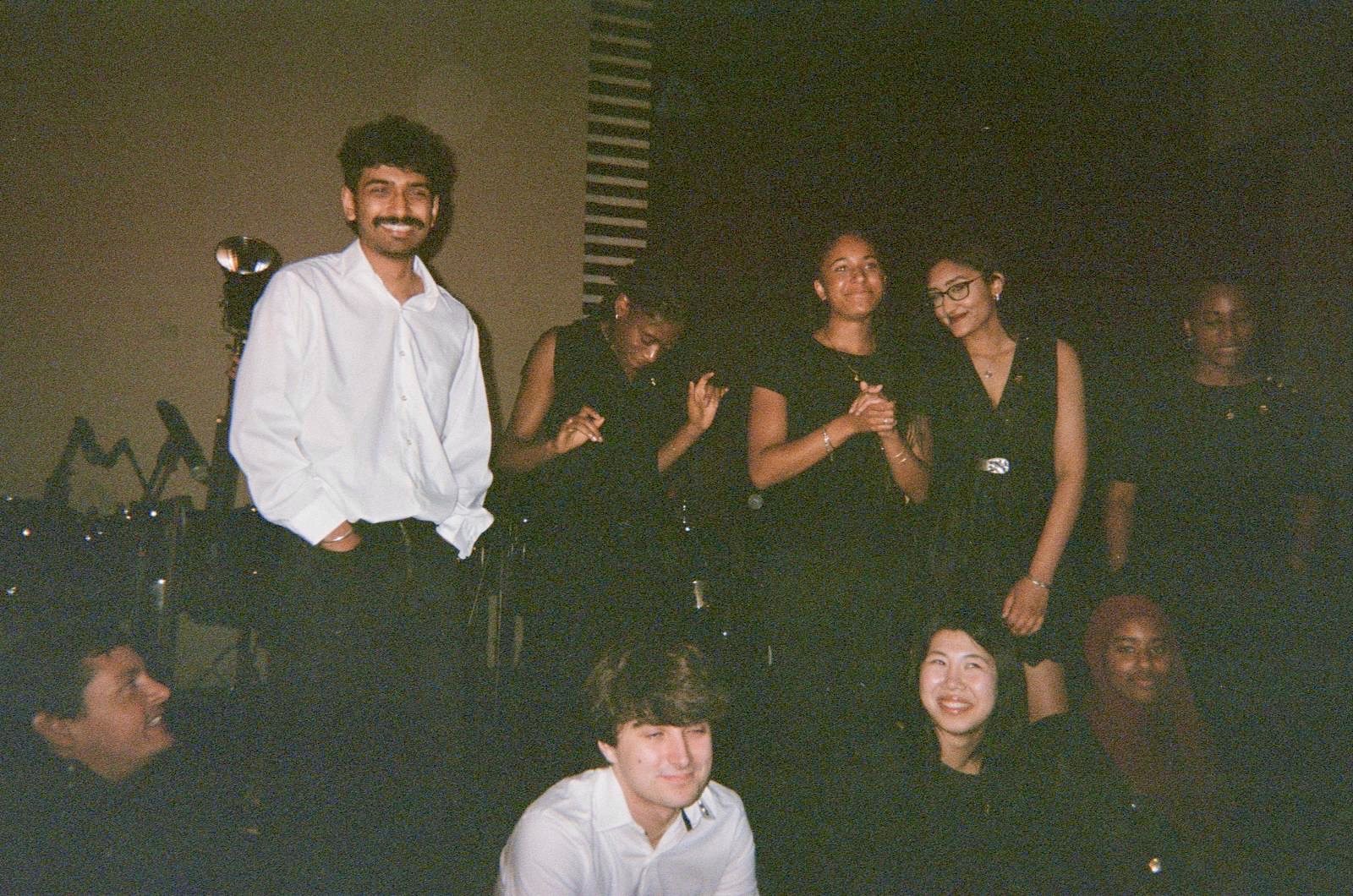 Ensemble members in concert dress talking and laughing together in low light before the show.