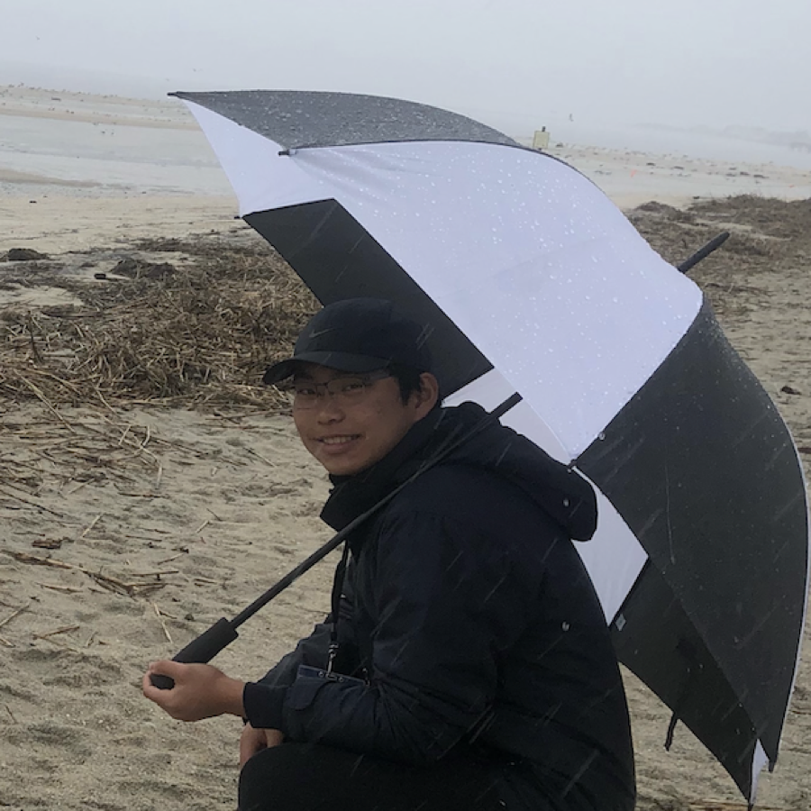Luke Tan holding an umbrella on a beach