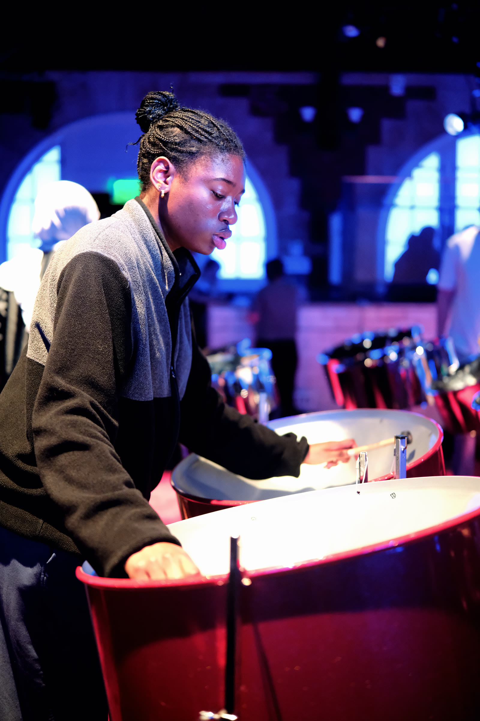 An ensemble member practicing her part on steelpan under stage lighting.