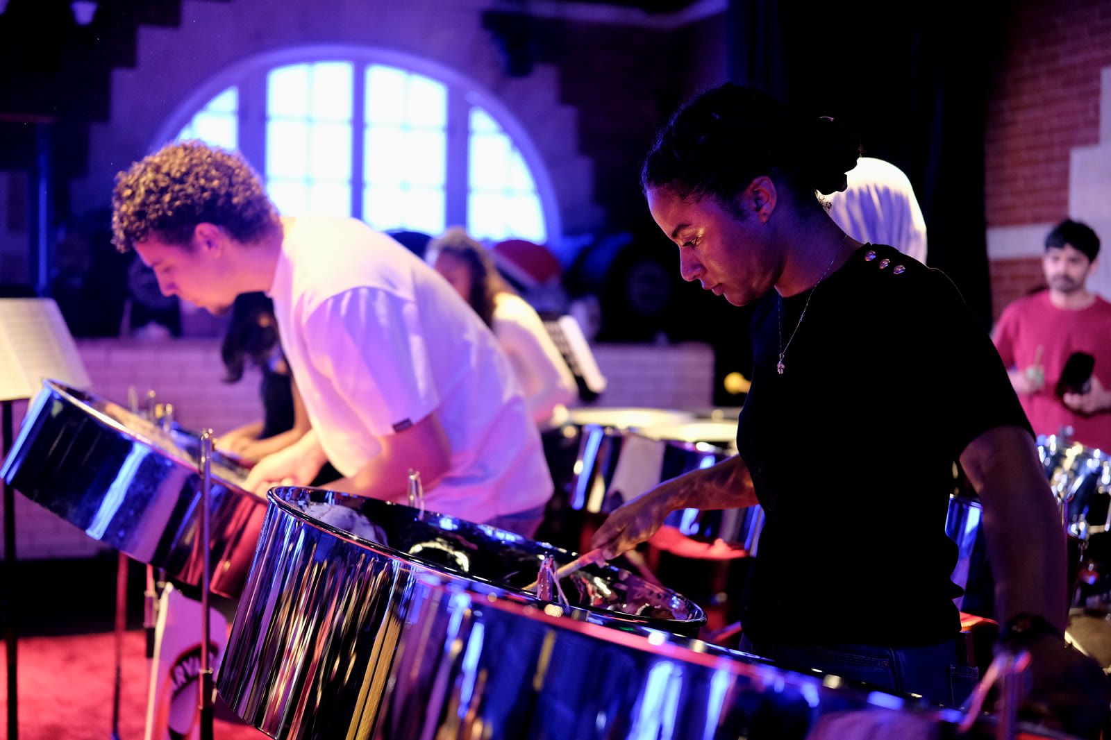 Two ensemble members concentrating as they play steelpans during rehearsal.