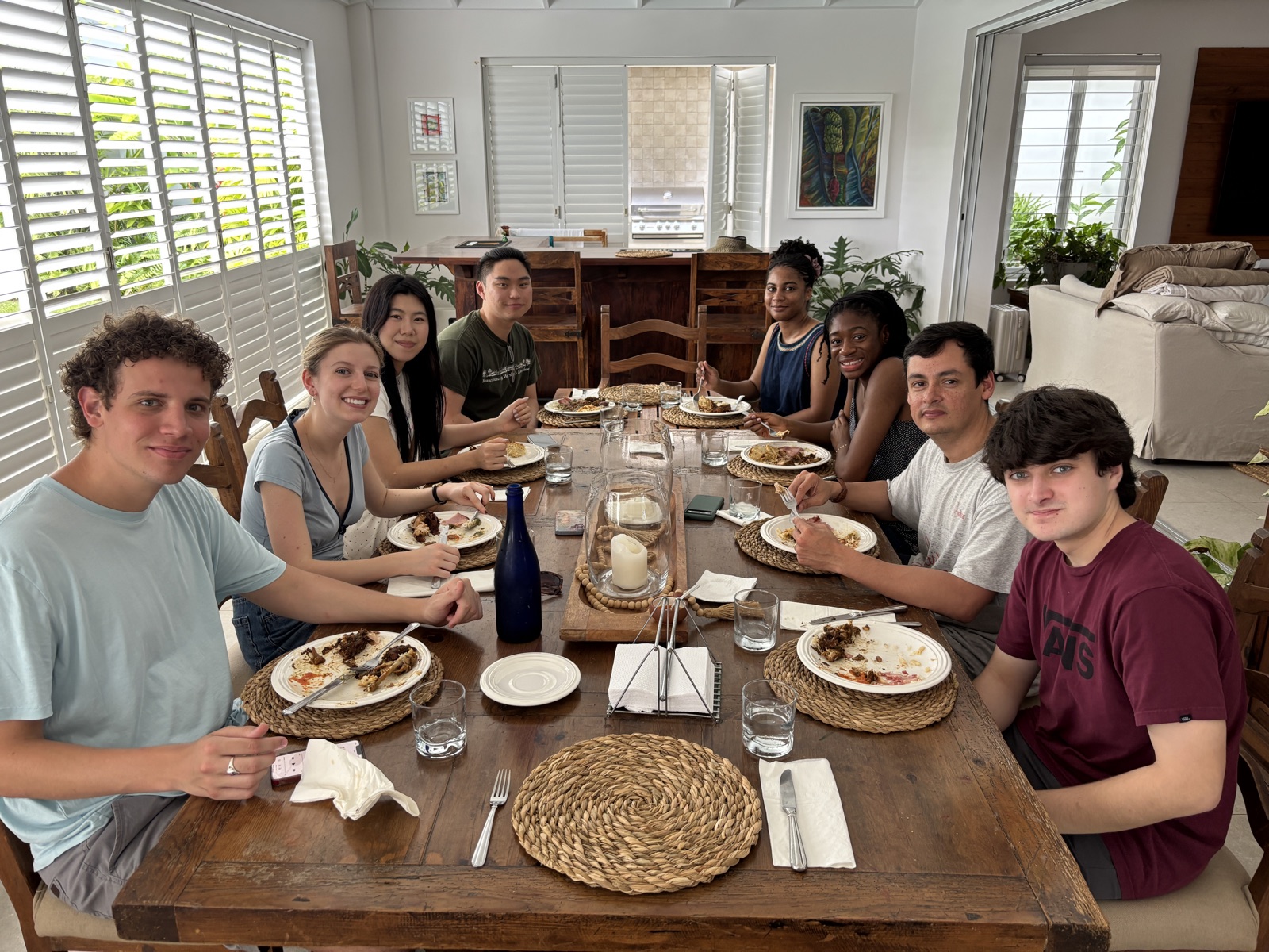 Ensemble members around a long wooden table over lunch, plates cleared.